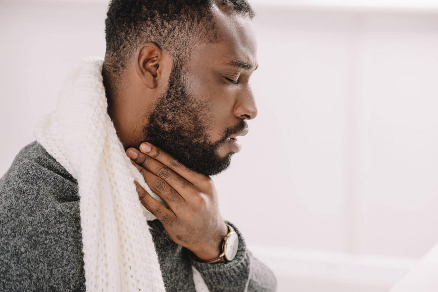 laryngitis-hoarseness Side view of a man holding his throat with his mouth slightly open.