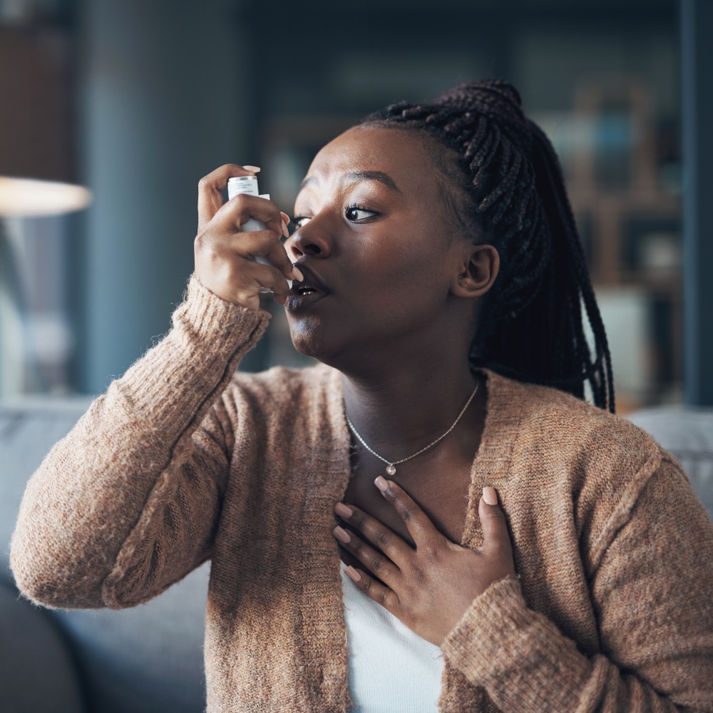 a uses an asthma inhaler while sitting on a couch indoors
