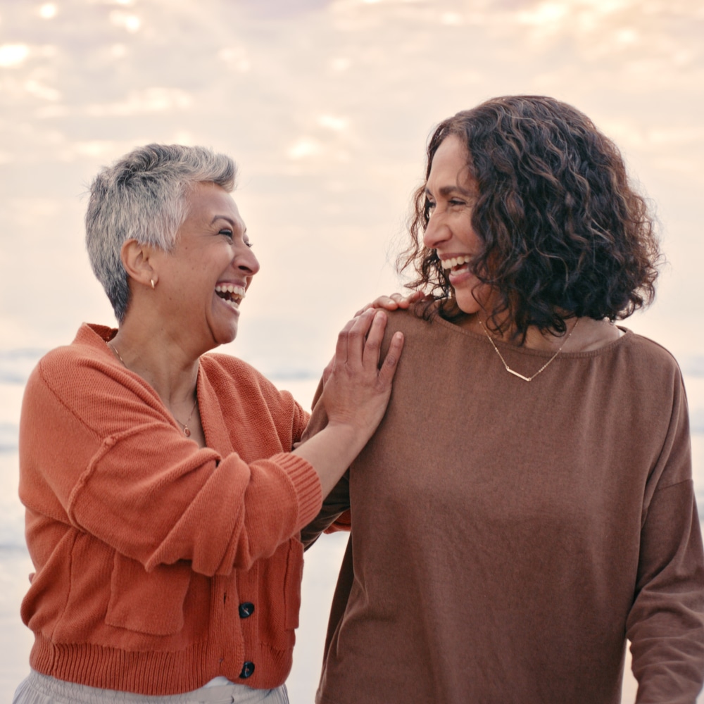 two women smile at one another in conversation outdoors